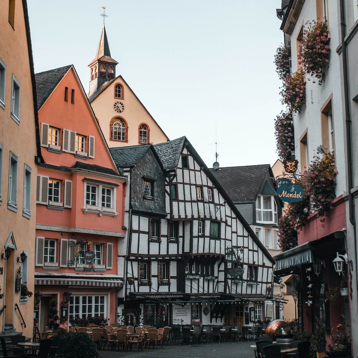 Home 8 Eine malerische Europastraße in Bernkastel-Kues mit charmanten Fachwerkhäusern, farbenfrohen Fassaden, Blumenkästen, Sitzgelegenheiten im Freien und einem Kirchturm unter freiem Himmel - das ist eine gemütliche, einladende Szene in dieser kleinen historischen Stadt.
